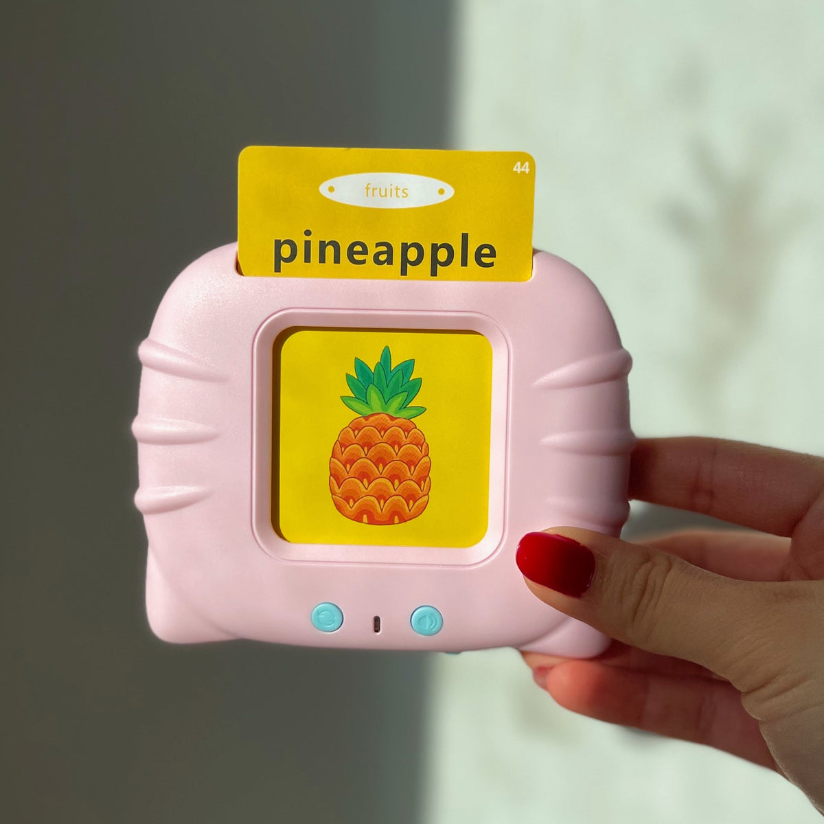 Pink PocketSpeech USA talking flashcard reader held in hand, displaying a "pineapple" flashcard from the fruits category
